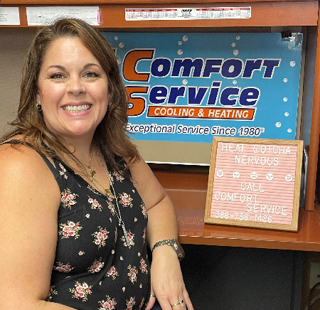 Sandra Lumberry next to a board with the orange and blue Comfort Service logo.